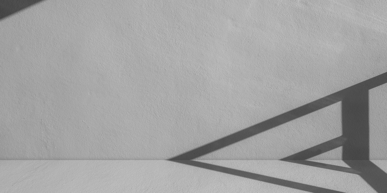 A white wall in strong sunlight with the sharp triangular shadow of a railing across it.